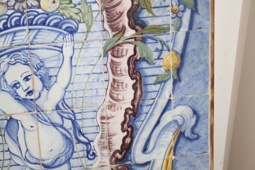 A Continental maiolica tile panel, depicting a putto holding aloft a basket of fruit, overall 90 x 72cm